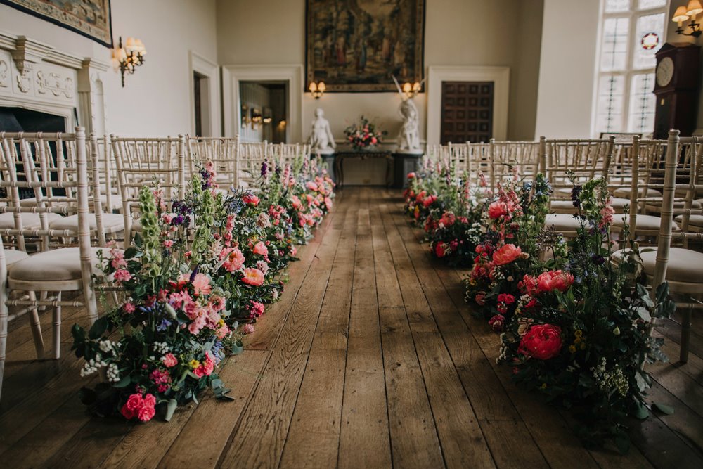 Bright pink flowers decorate an aisle for a wedding ceremony in a beautiful stately home in the cotswolds