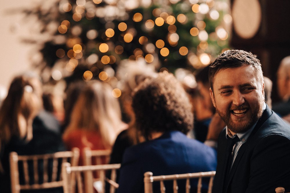 best man smiling in front of christmas tree waiting for wedding ceremony to begin