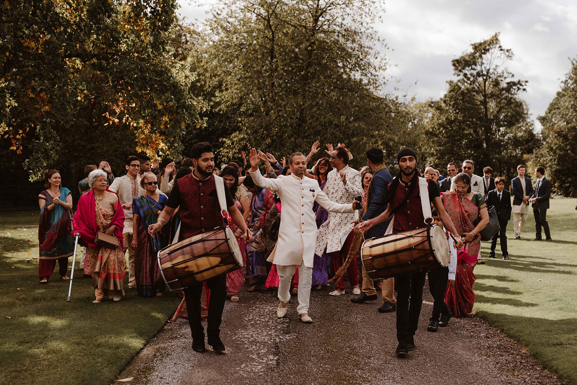Baraat procession for arrival of the groom with dhol drummers and dancing walking along driveway at indian wedding venue elmore court