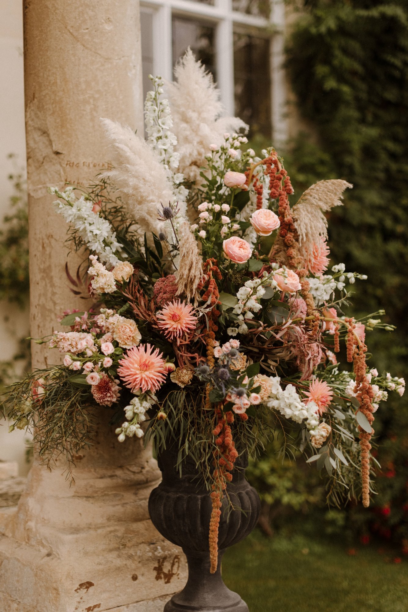 Boho luxe pink and white september wedding flowers in urn outside stately home venue in cotswolds