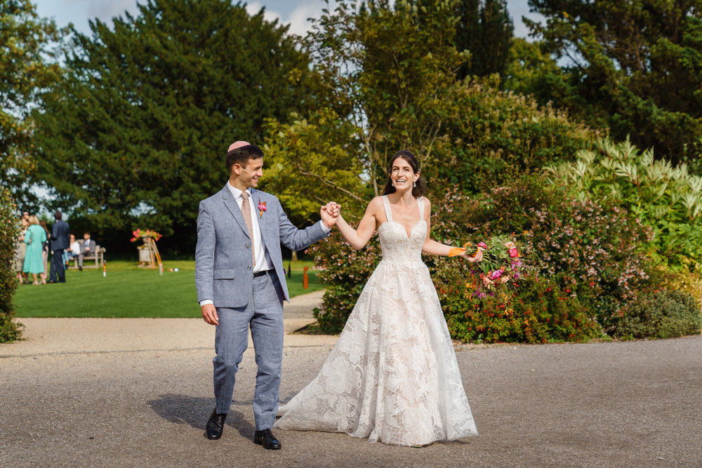 Newlywed Jewish Bride and groom holding hands and grinning 