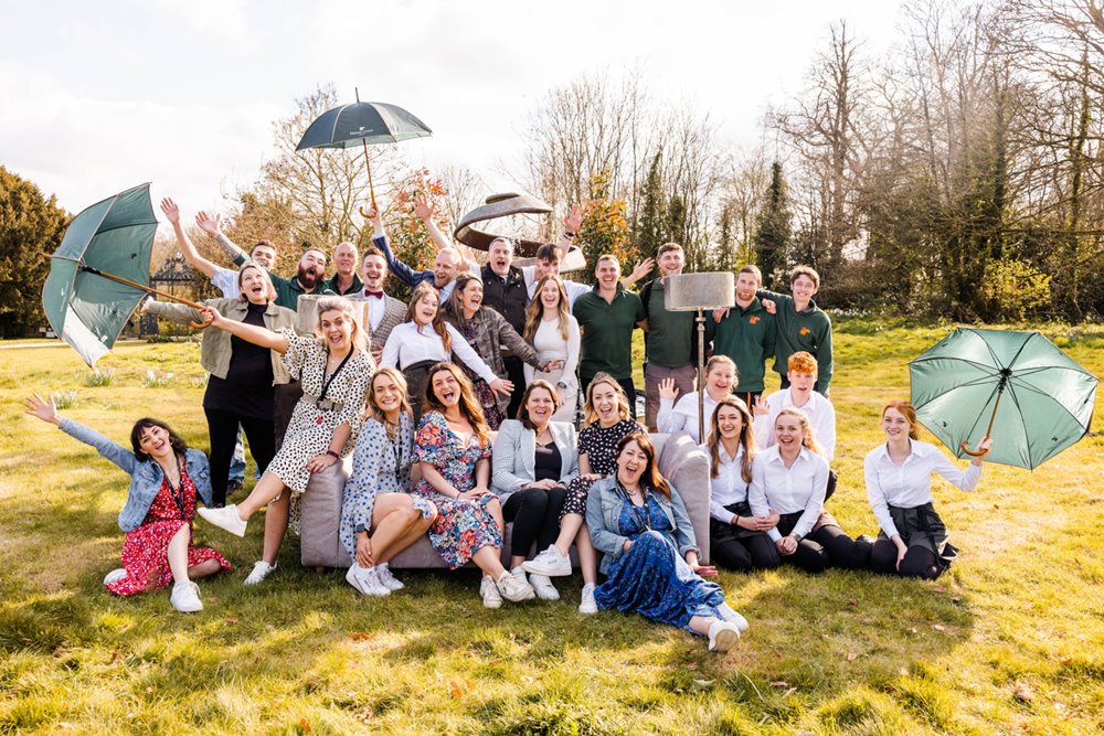 Team E at Elmore Court holding umbrellas and posing in Friends recreation for a fun photoshoot at their unusual wedding venue open day in 2022