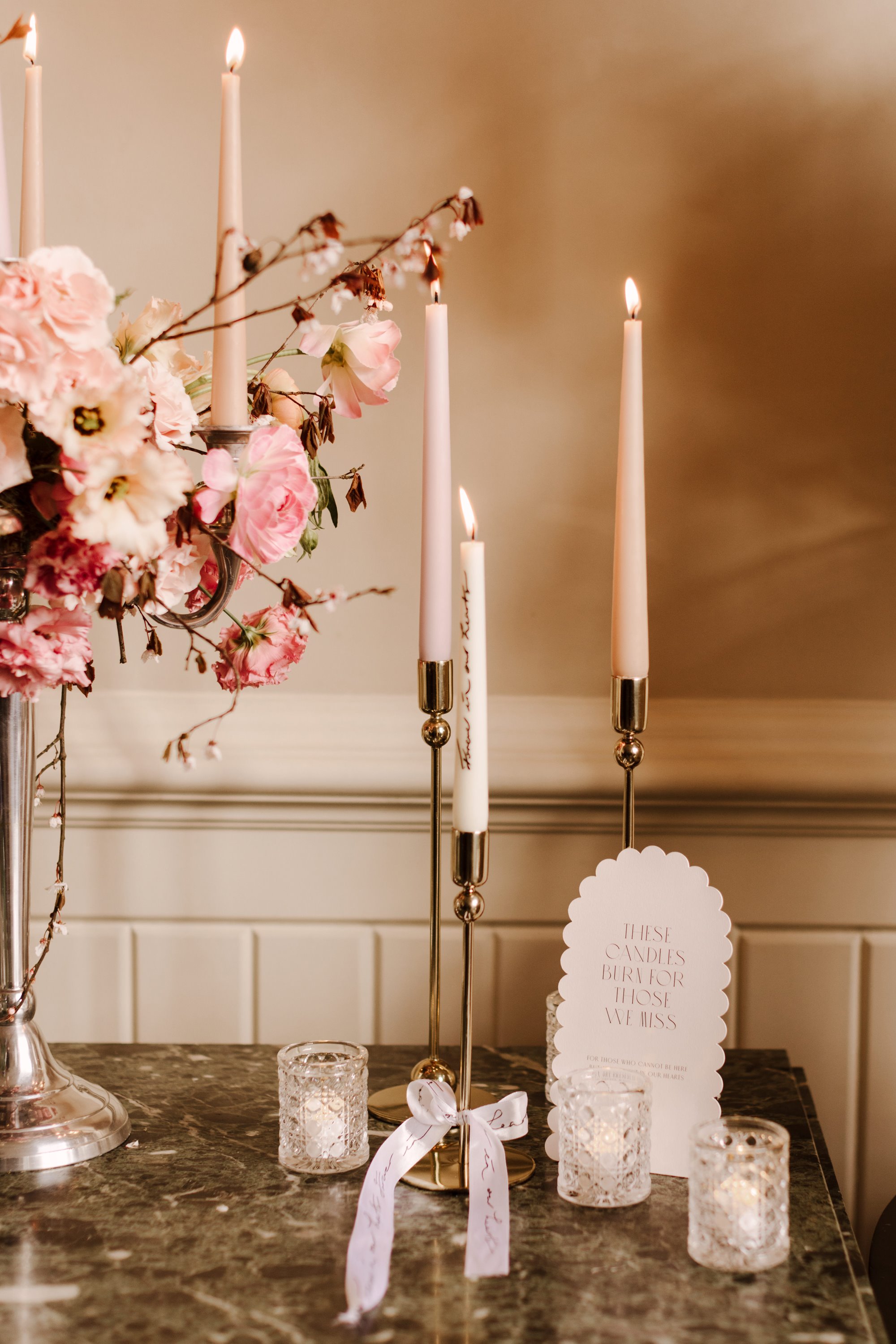long and sleek candles flicker on a dressed table of pink and white flowers 