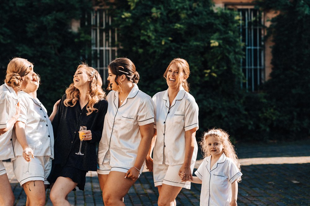 bridal party and flower girl in pyjamas with champagne outside stately home wedding venue on an autumn wedding morning