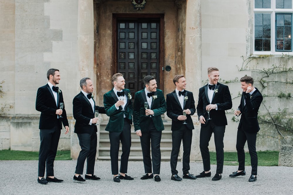 Groomsmen in green velvet suits have fun posing outside their stately home wedding venue