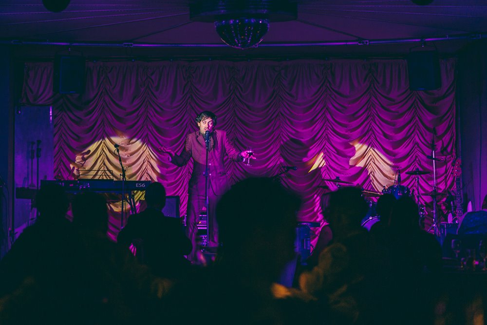 Alternative comedian almost blends into the purple curtains wearing his purple suit onstage