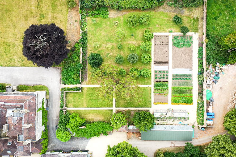 Ariel view of a kitchen garden full of vegetables, a greenhouse and a small orchard of fruit trees 