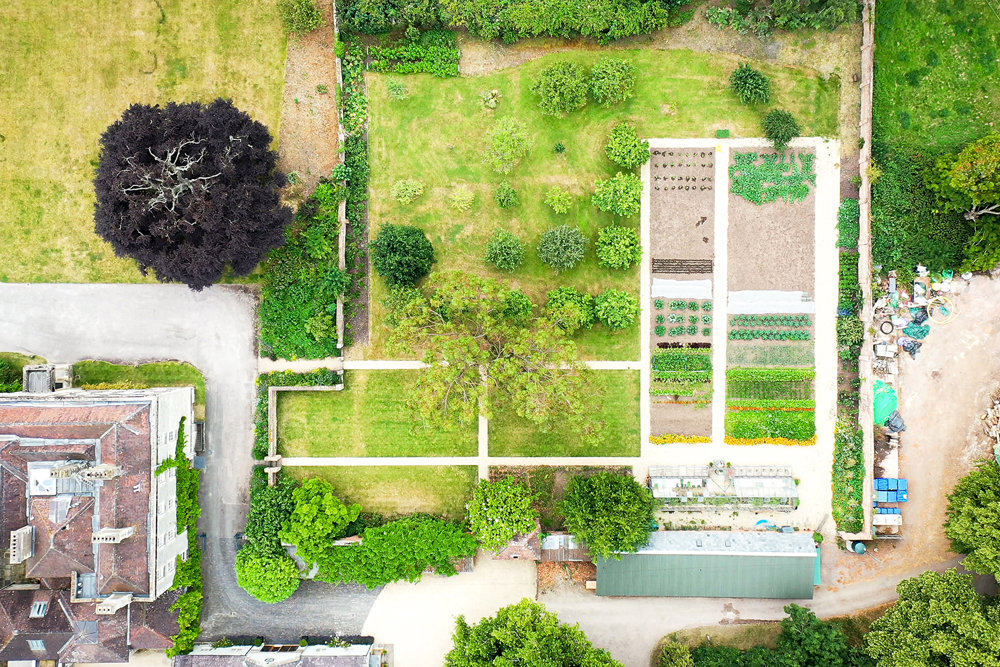 Ariel view of a kitchen garden full of vegetables, a greenhouse and a small orchard of fruit trees 