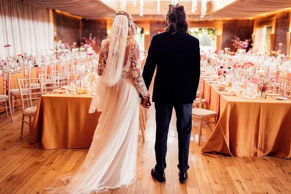 Cool bride and groom holding hands looking at their fun colourful wedding reception for the first time in an eco party venue in gloucestershire