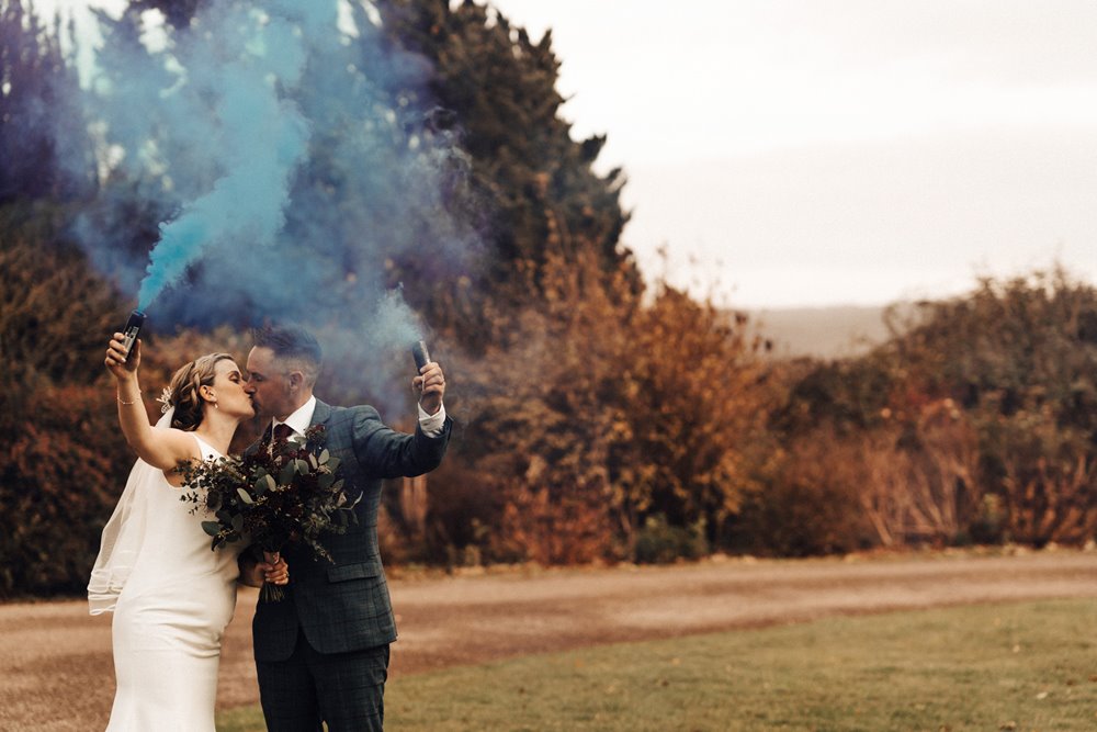 couple hold surprise gender reveal for their wedding guests with blue smoke bombs