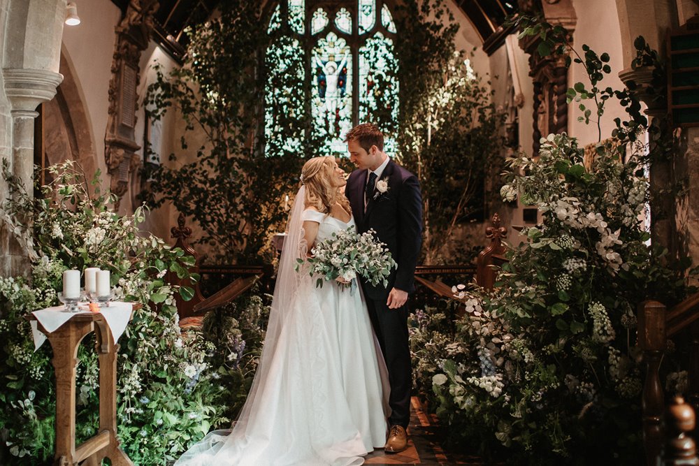 Bride and groom look lovingly at each other at their beautiful church wedding ceremony in England's prettiest church in Elmore, Gloucestershire 