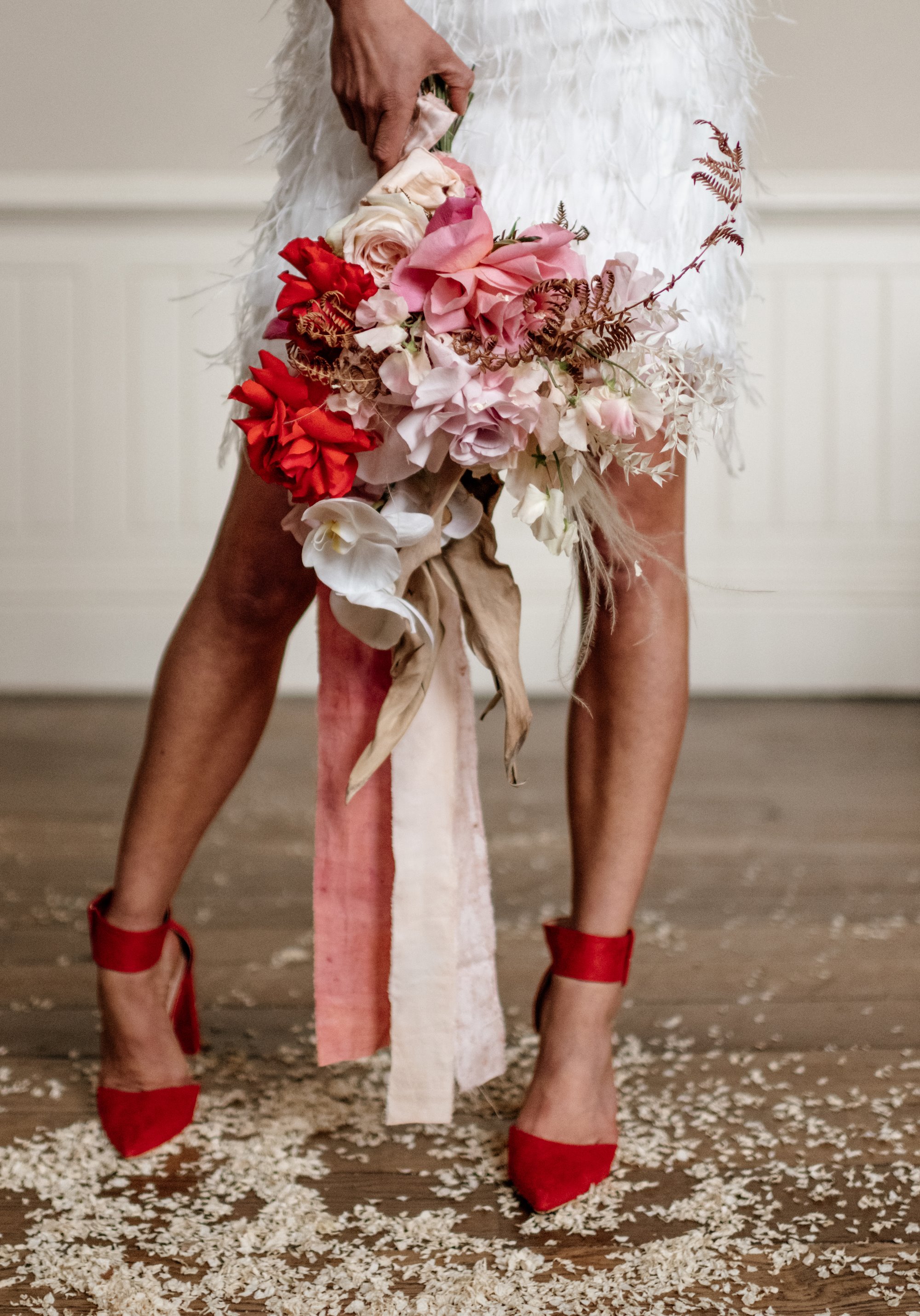 bride in bright red heels with a white dress, holding pink, red and white bouquet of flowers 