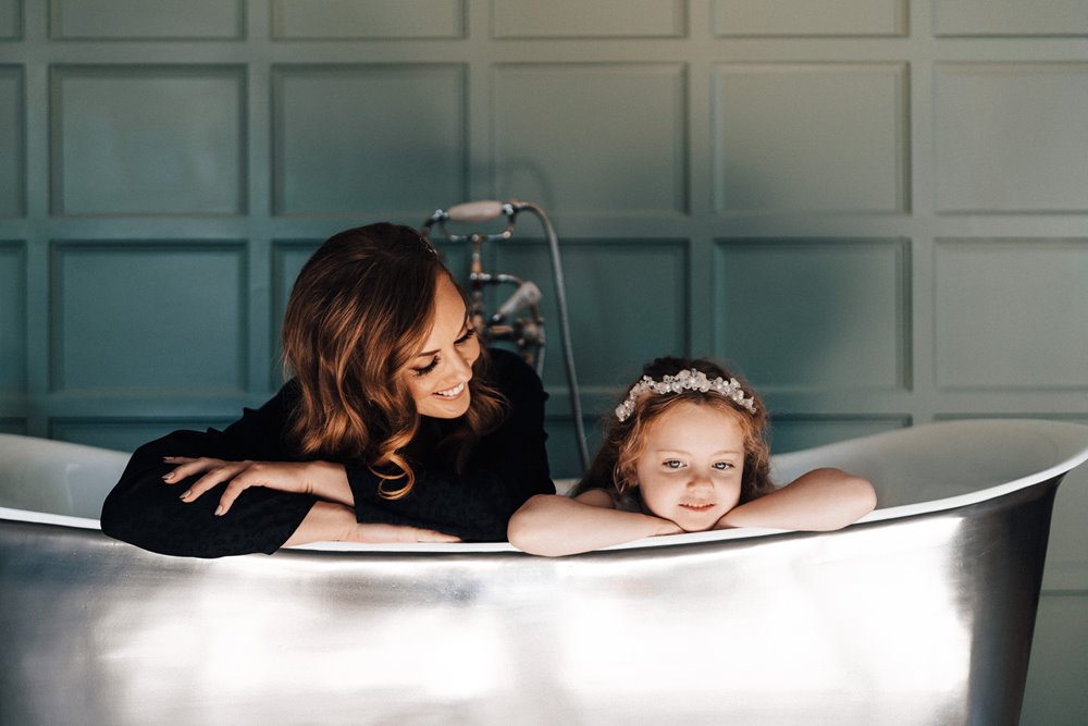 Bride poses with her daughter in a big bath on the morning of her wedding at an english country house in october