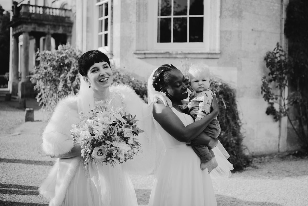 Happy newlywed brides pose for photos outside mansion house wedding venue after their same sex ceremony at elmore court