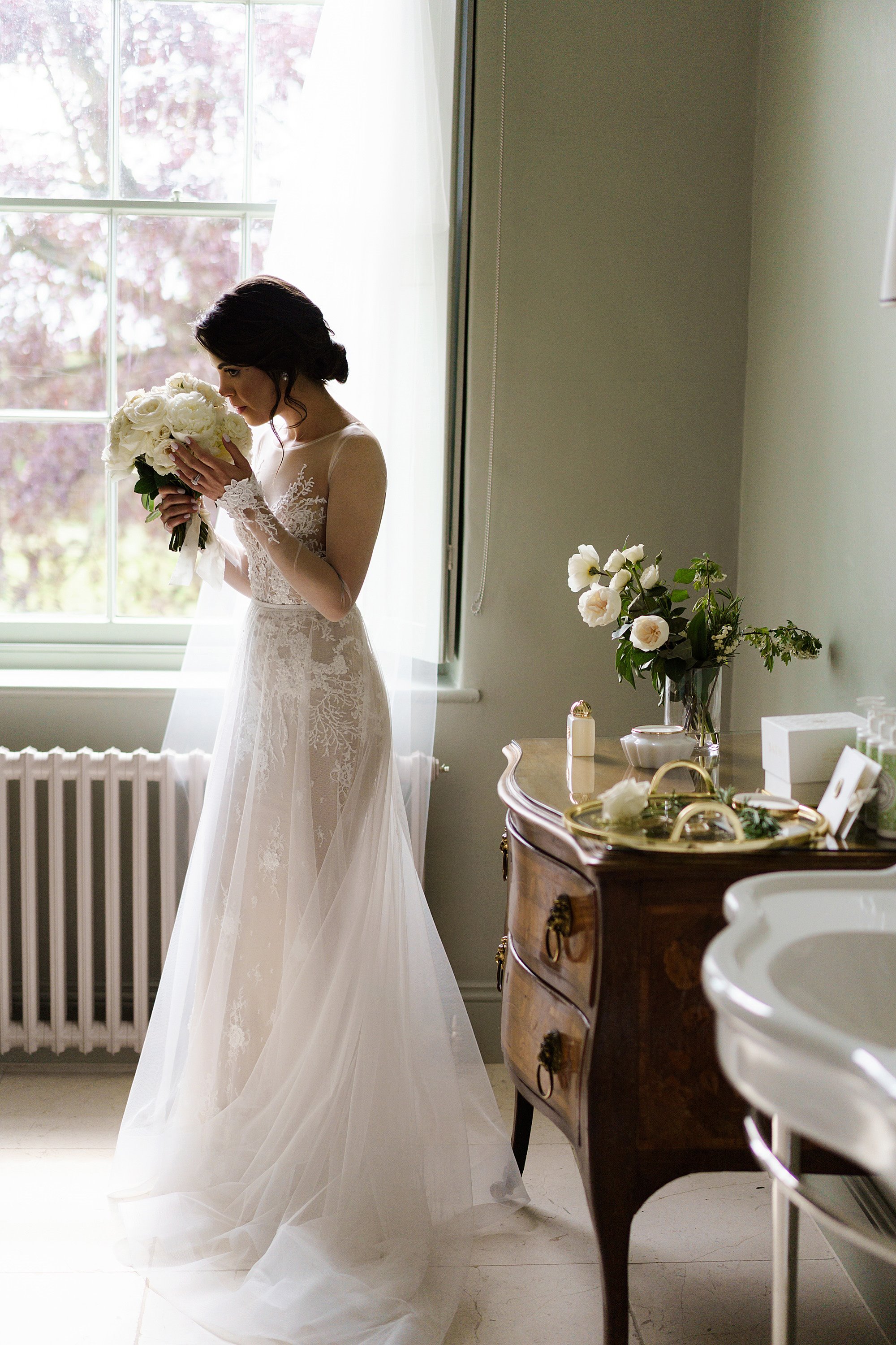 A bride just ready in her wedding dress having just been handed her bridal bouquet, she takes a moment to smell the roses and have a deep breath of beautiful scent before she sees her husband to be for the first time