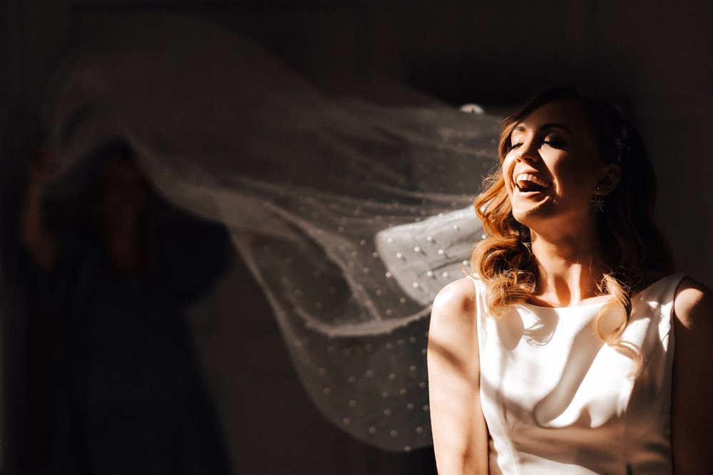 Beautiful bride laughs in magical autumn light wearing long pearl studded veil at her October wedding in the cotswolds