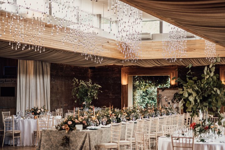 Beautiful Wedding reception with light installation decorated with september florals and fruits on a mix of long and round tables for a wild wedding fair Harvestival at elmore court in Gloucestershire