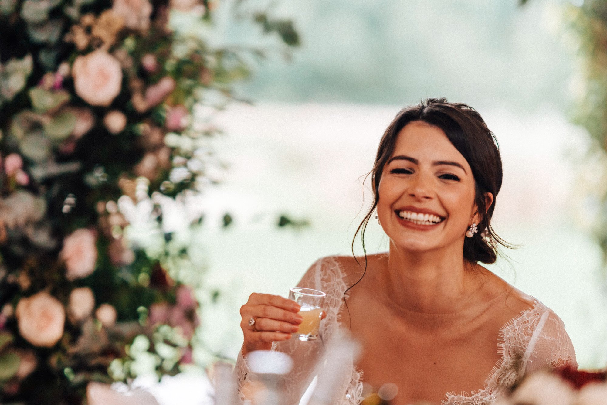 Beautiful bride in pearl earrings grins holding shot glass 
